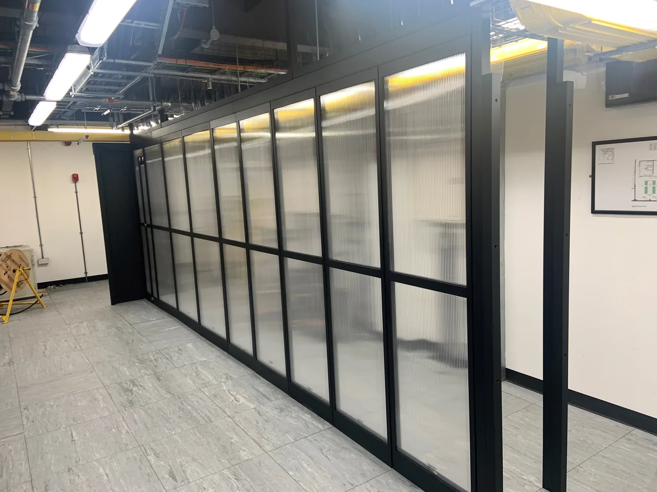 Long run of black framed translucent containment panels inside a technical room