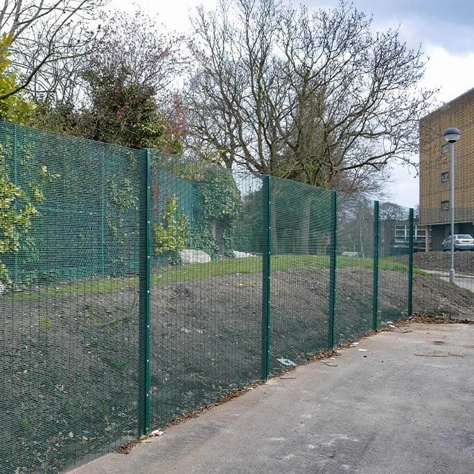 Green mesh fencing following a planted boundary beside a building