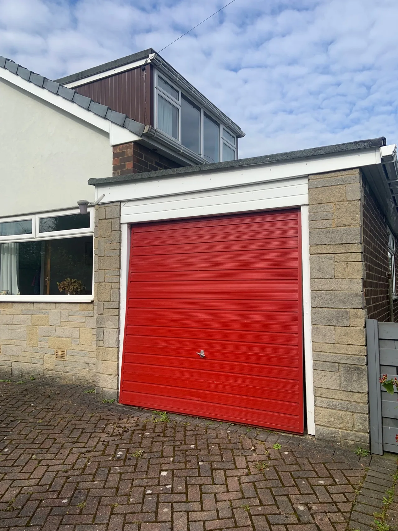 Red garage door beside a white house, before replacement.