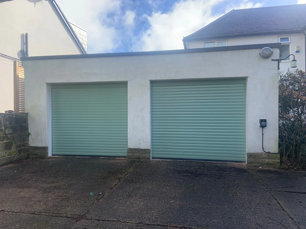 Two pale green roller garage doors fitted to a white rendered building
