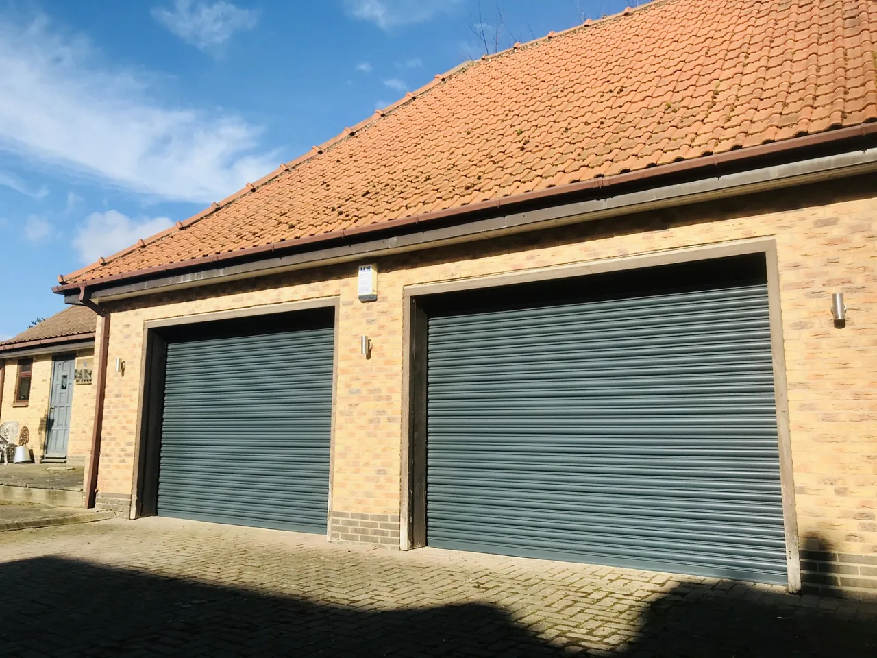 Two grey roller garage doors below a red tiled roof