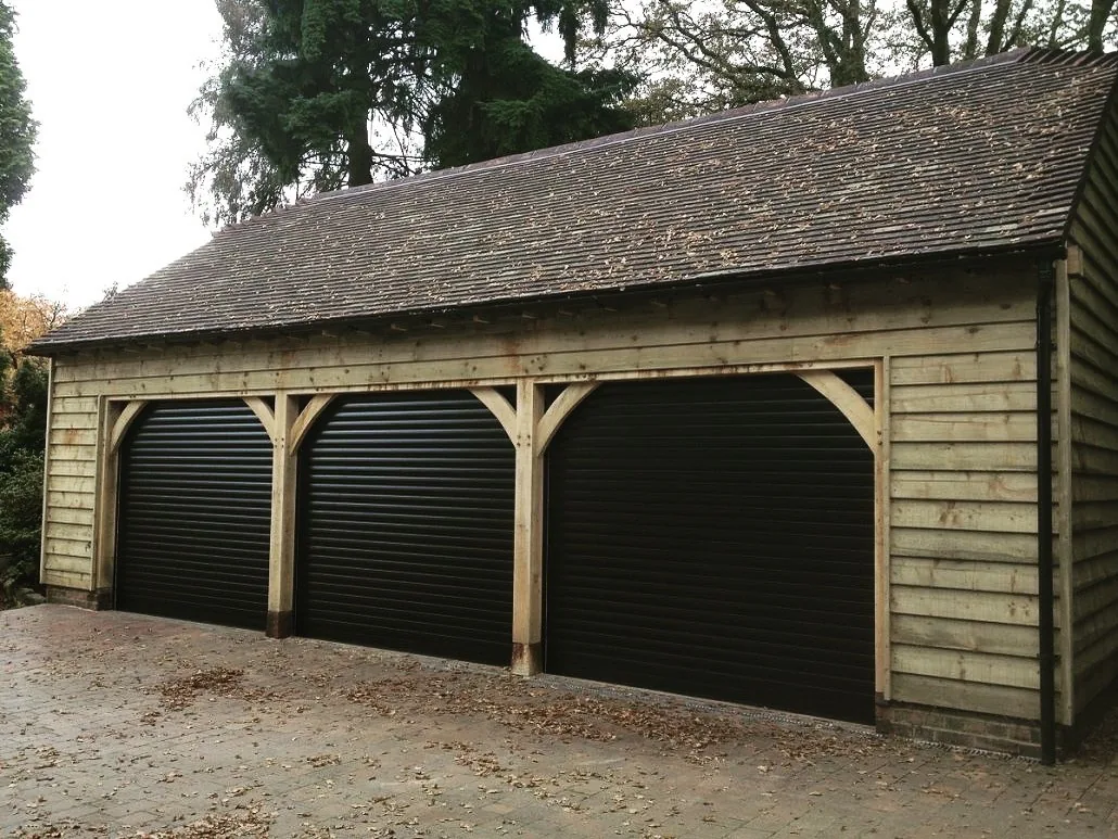 Three dark roller garage doors set into a timber garage building
