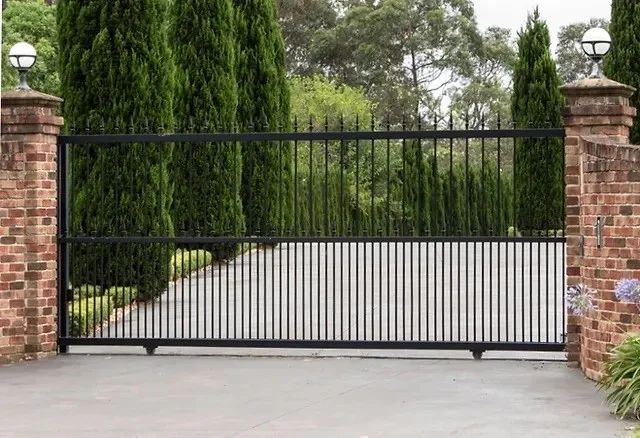 Sliding gate with black railings and pale solid lower panels between brick pillars.