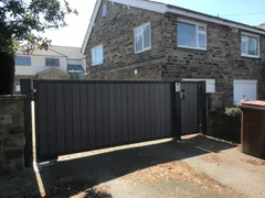 Dark infill driveway gates between stone posts outside a house