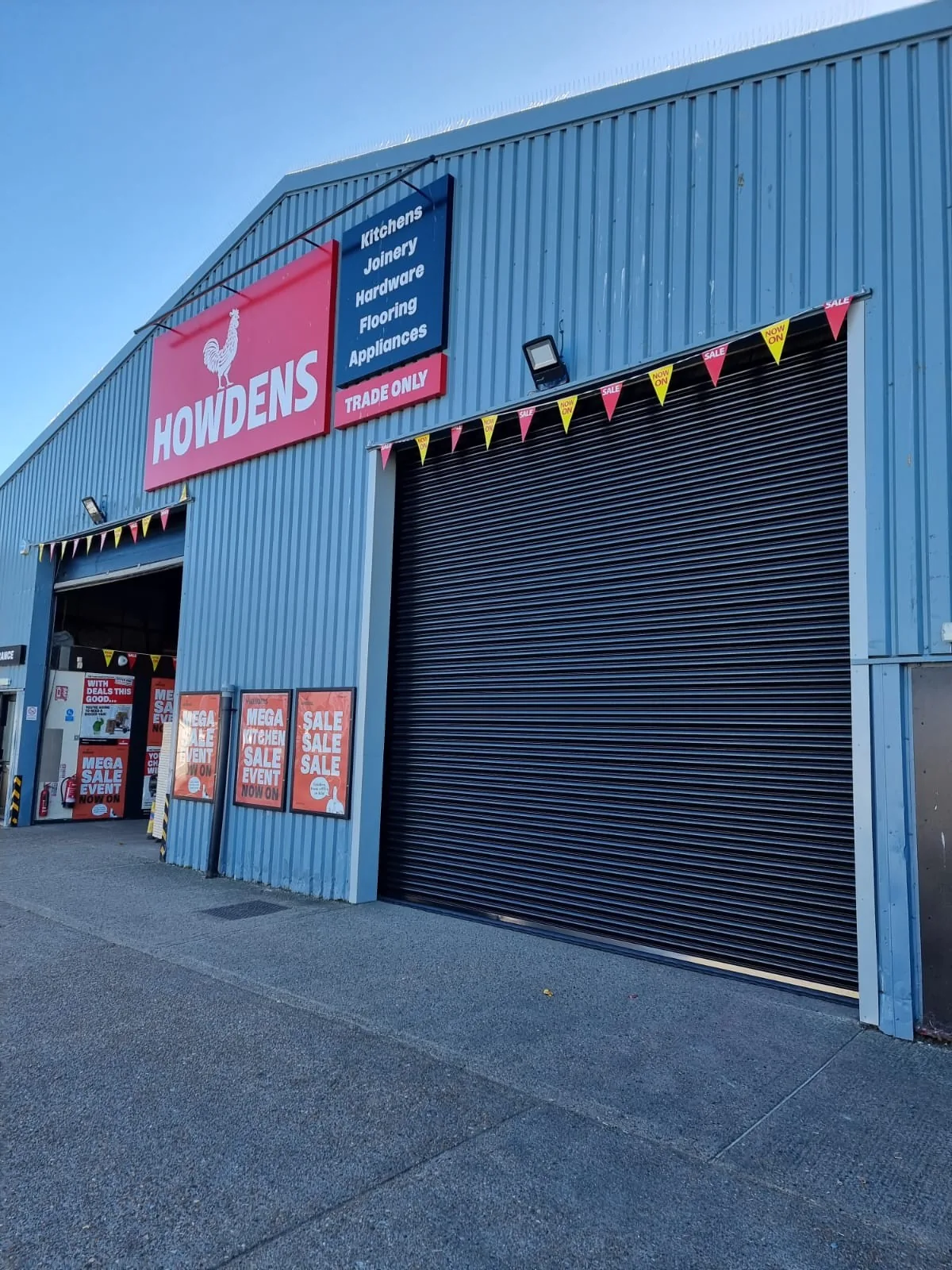 Dark roller shutter beside a trade counter entrance on a blue-clad building.