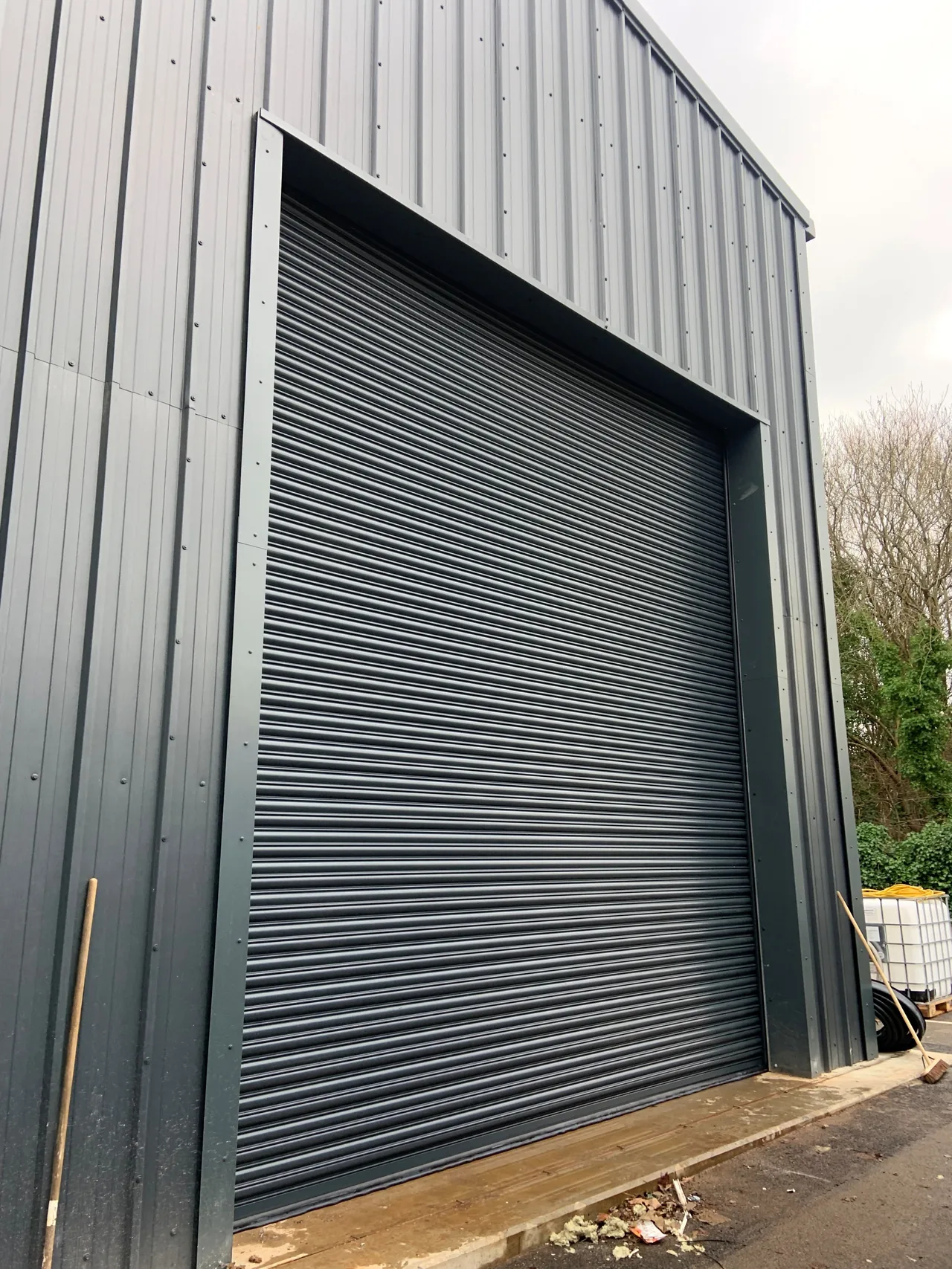 Dark roller shutter within a grey metal-clad industrial building.