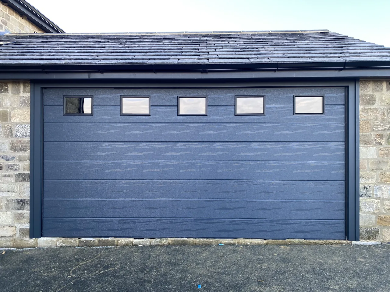 Wide grey sectional garage door with rectangular upper windows