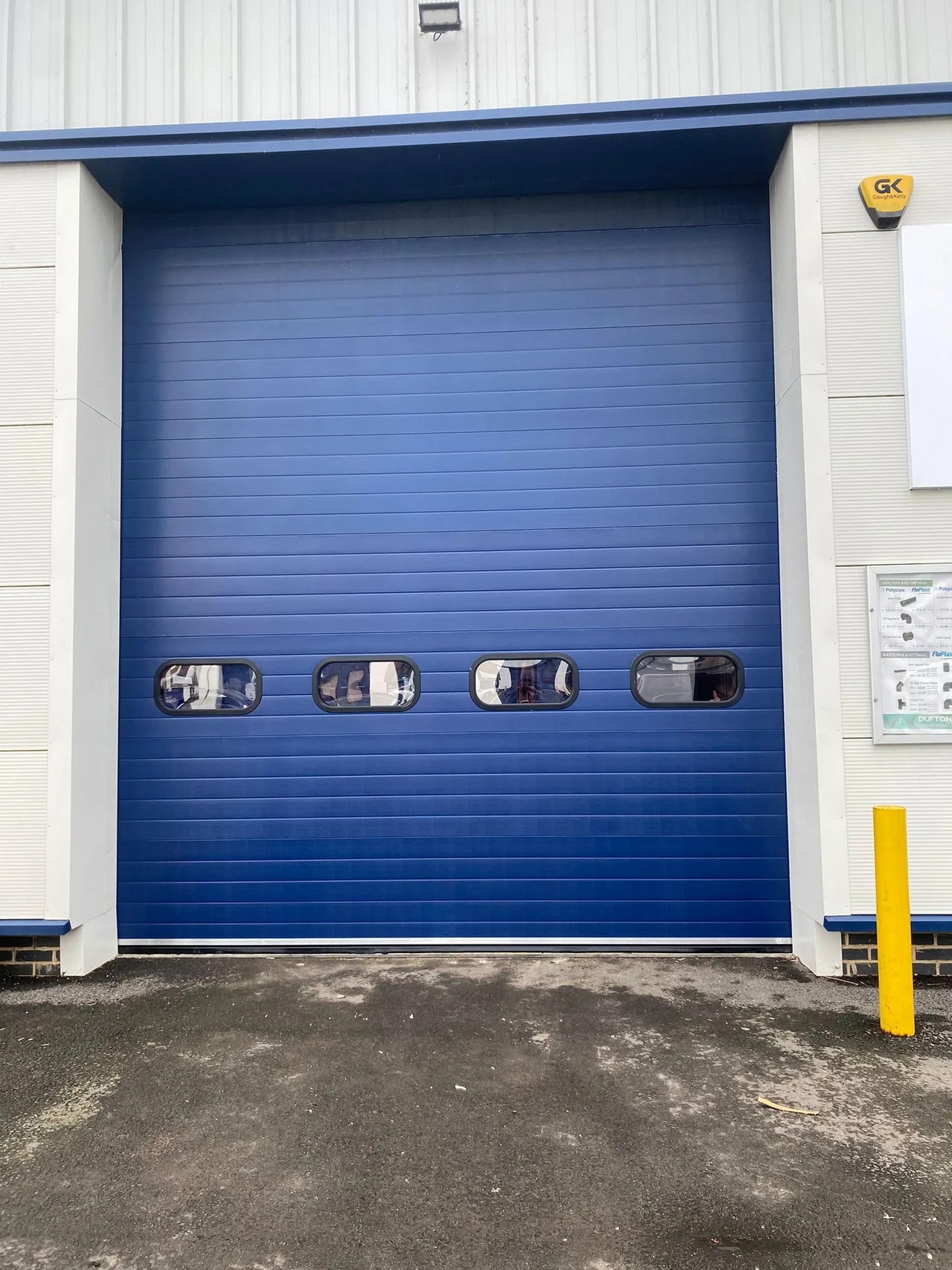 Blue sectional door with straight panels and four windows across the warehouse opening.