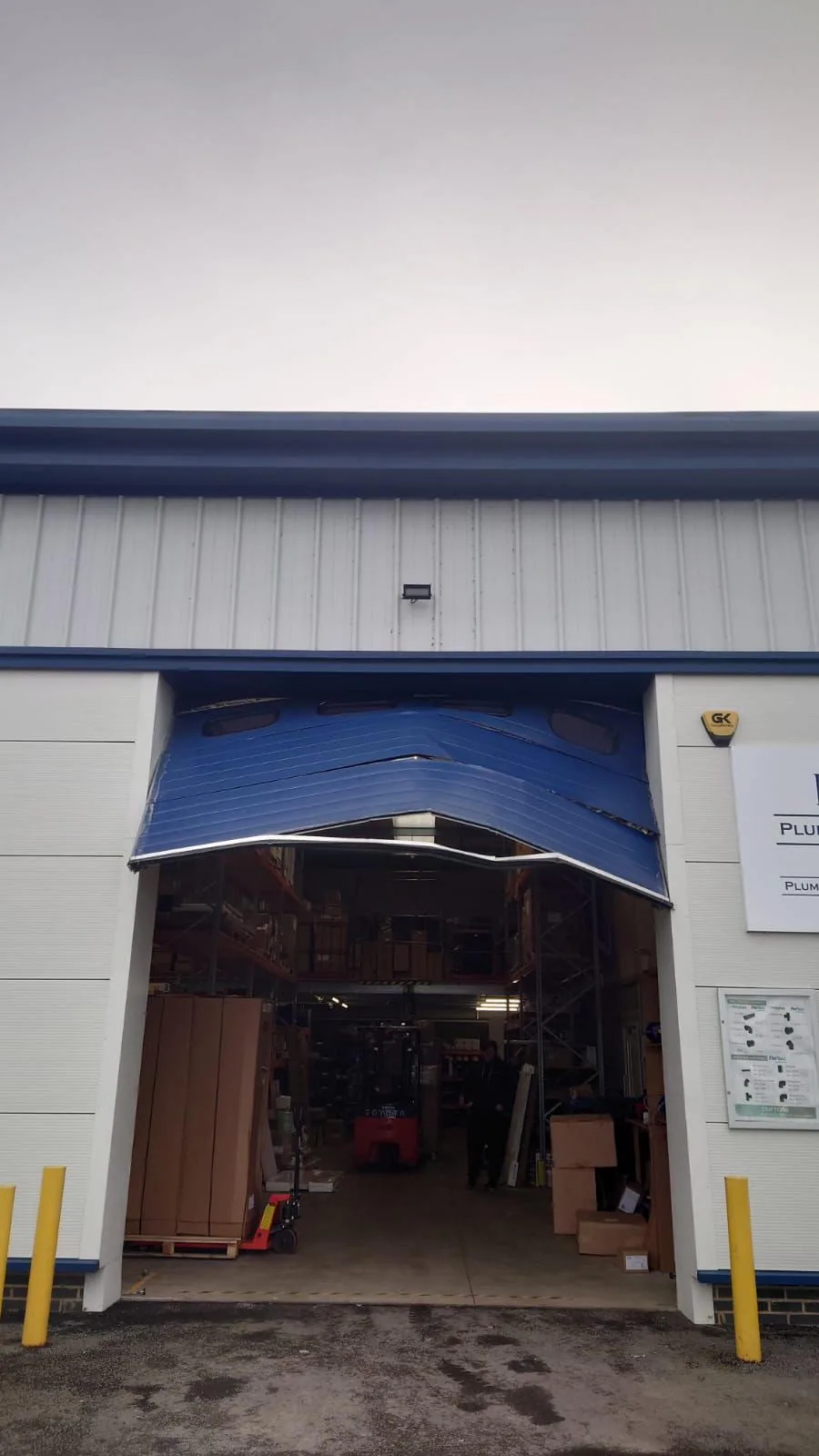 Buckled blue sectional door raised above a warehouse opening.