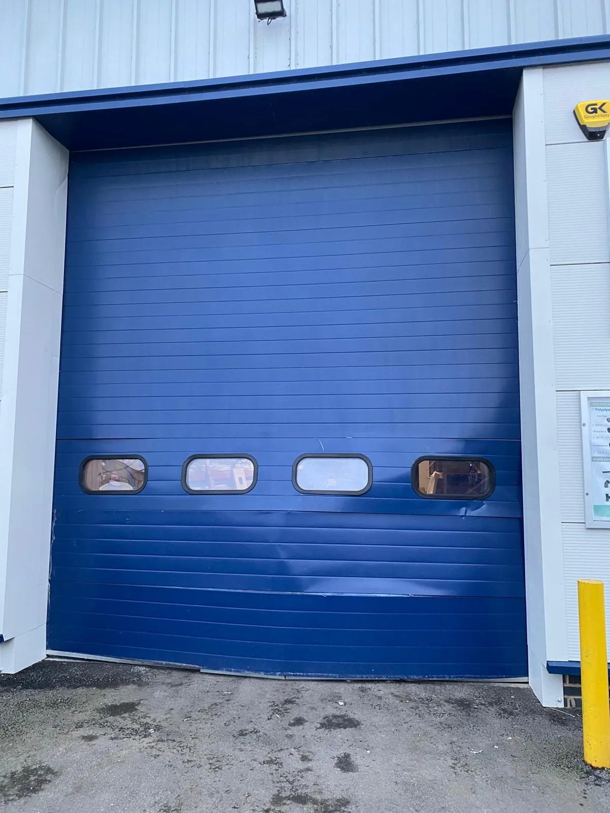 Closed blue sectional door with dented lower panels and four windows.